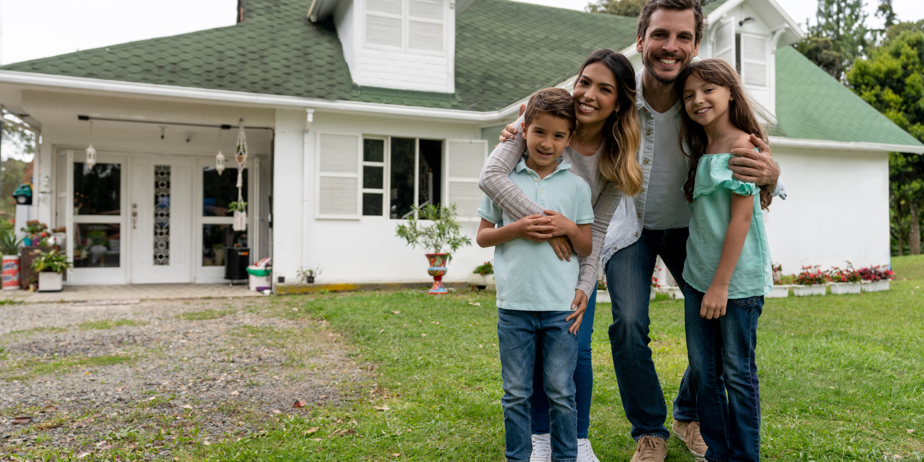 Family with arms around each other smiling in from of their home