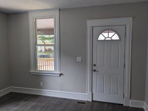 Living room door and window. Wood floors and and white trim. Window looks out over porch and yard.